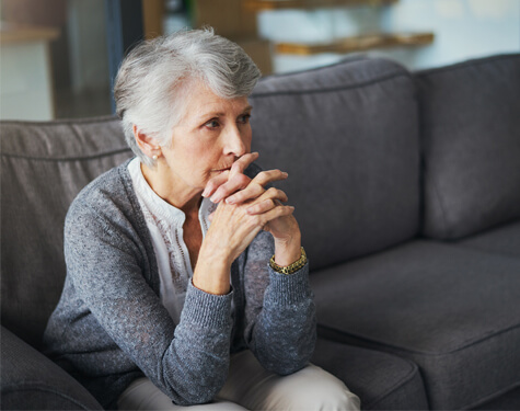 Elderly woman sitting on couch while clasping hands